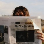 A person reads The New York Times outside on a sunny day, capturing a moment of leisure. — Crypto casino on mobile