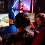 Two gamers engaged in a heated video game session surrounded by neon lights and computer screens. — Vivatbet Sportsbetting: B