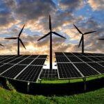 Wind turbines behind solar panels during sunset