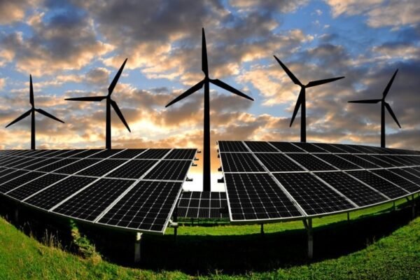 Wind turbines behind solar panels during sunset