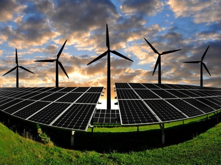 Wind turbines behind solar panels during sunset